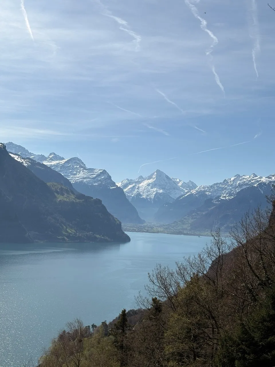 View over the deep-blue Urnersee between steep slopes toward snow-capped peaks and the broad Reuss valley.