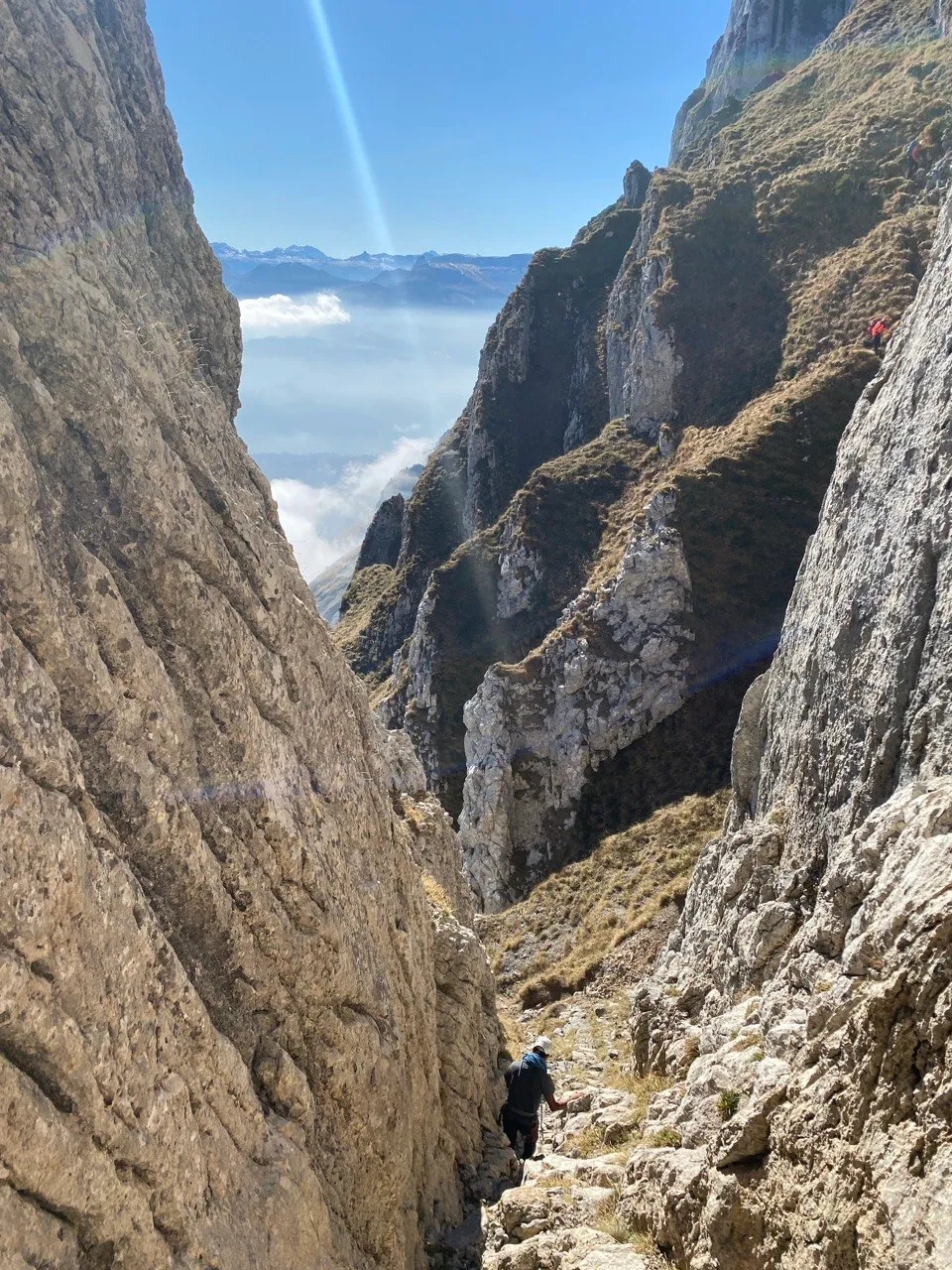 Looking up a steep rocky gully with a hiker climbing it, blue sky and distant ranges above.