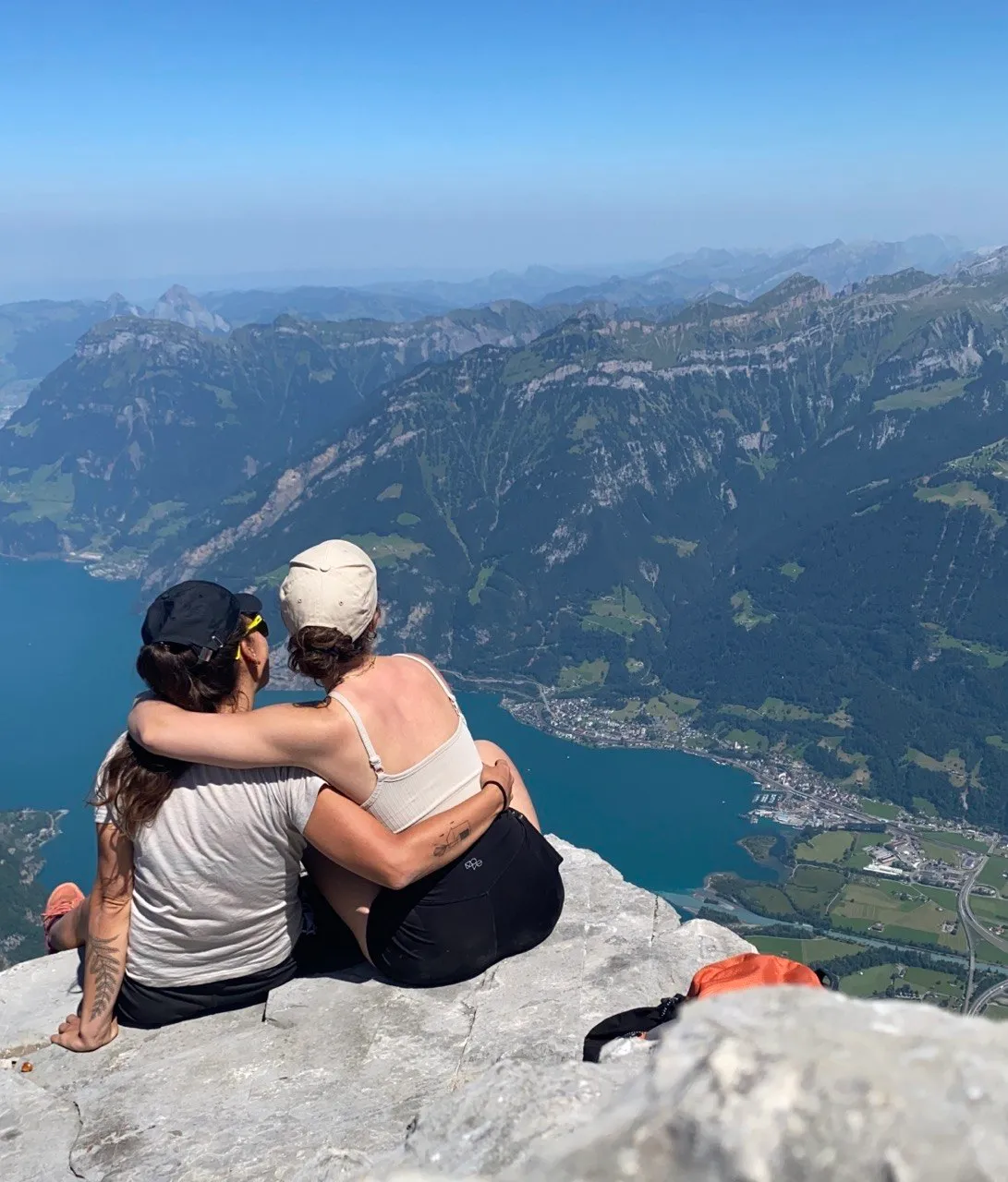 Two friends sit with arms around each other on the summit, taking in the view over Lake Uri.