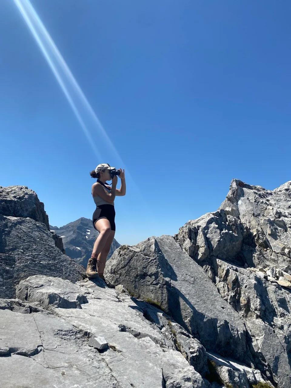 A hiker looks through binoculars on a rocky ridge.