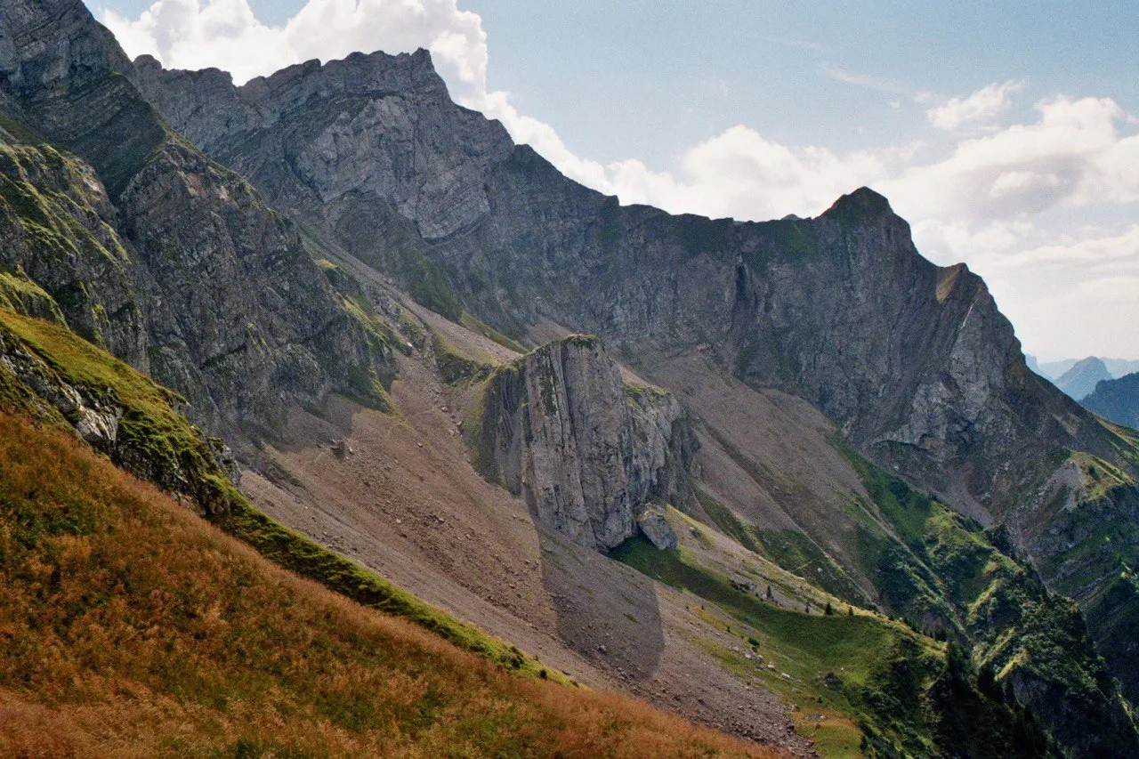A rugged limestone ridge of folded rock strata and scree fans, autumn-brown grass in the foreground.