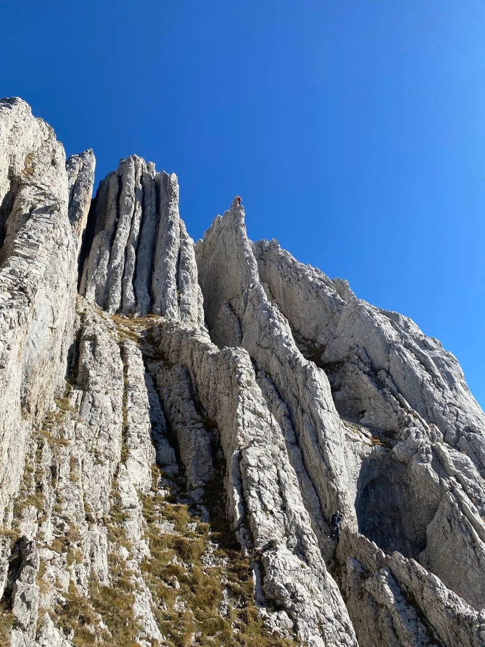 Jagged limestone fins and pinnacles against a deep blue sky, a tiny climber perched atop a spire.
