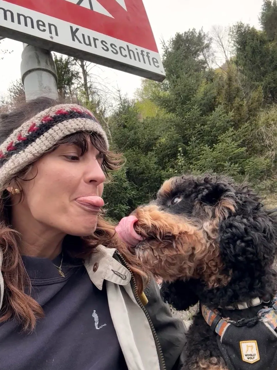 The same dog giving the hiker a lick on the chin under the Kursschiffe sign — a happy end to the day.