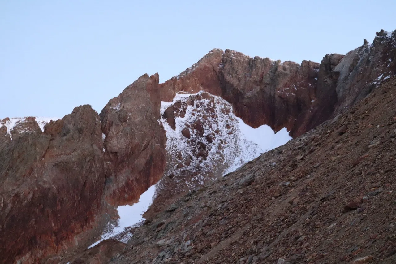 Alpenglow on glaciated peaks with a small frozen tarn below.