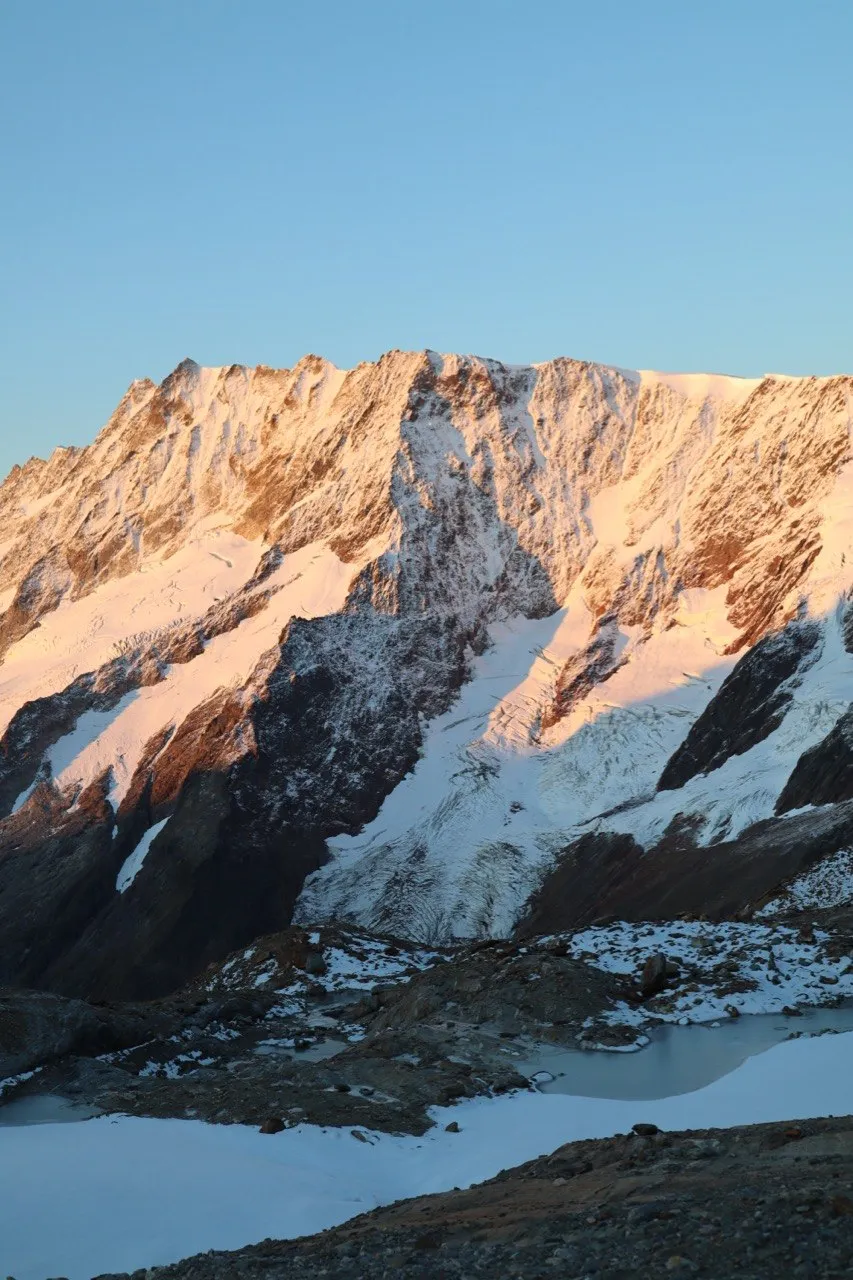 Red rock pinnacle with a patch of snow against a pale blue morning sky.