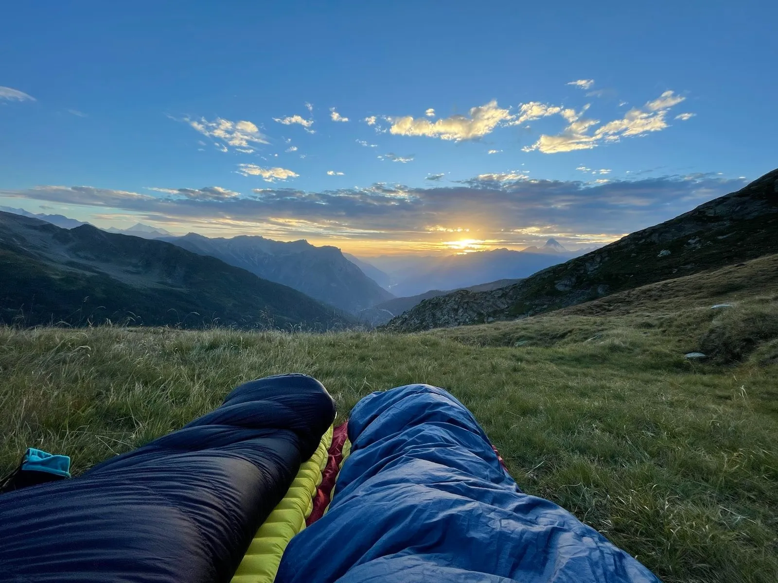 Sleeping bags on a meadow with the sun rising over the Alps.