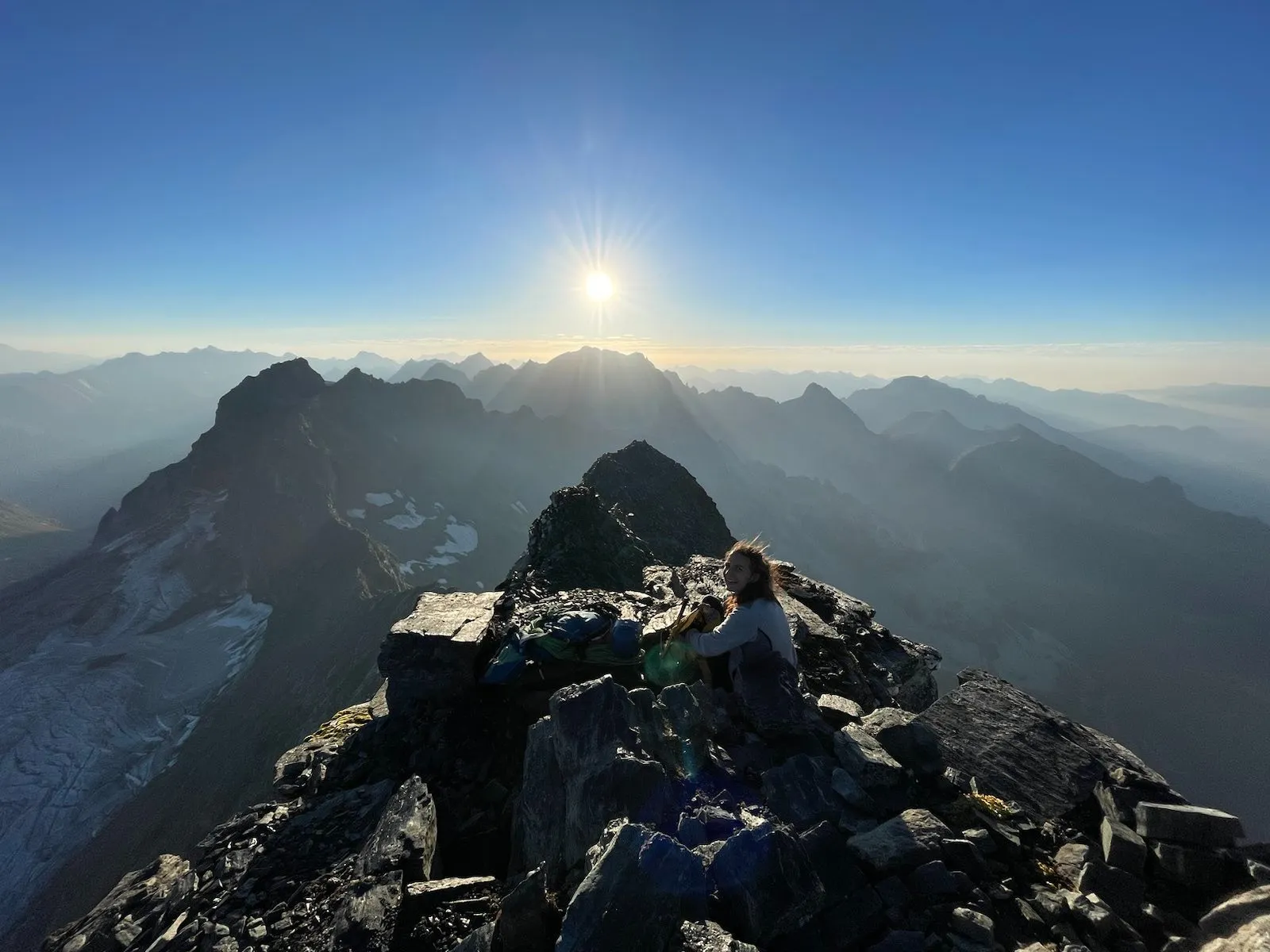 Sunrise from the Bortelhorn summit ridge with hazy mountain layers.
