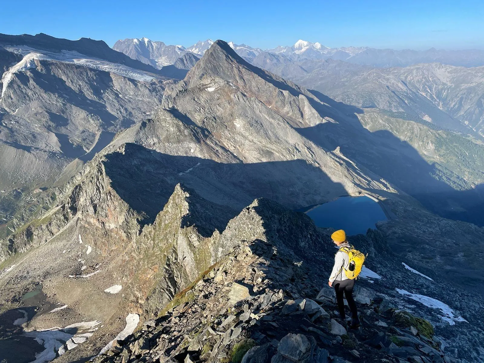 Descent ridge with a small alpine lake and snowy peaks in the distance.