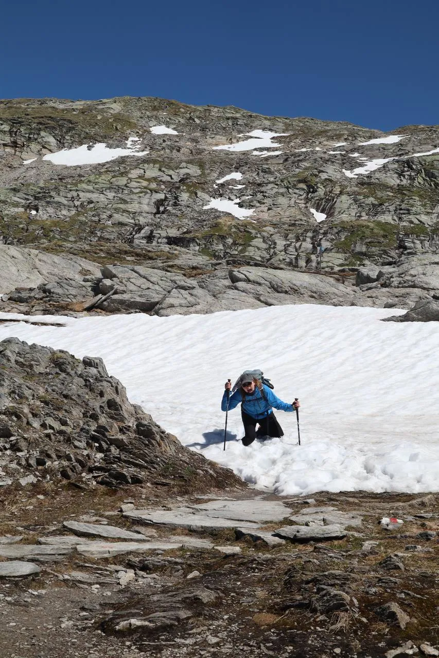 Hiker breaking trail up a steep snowfield below rocky slabs.