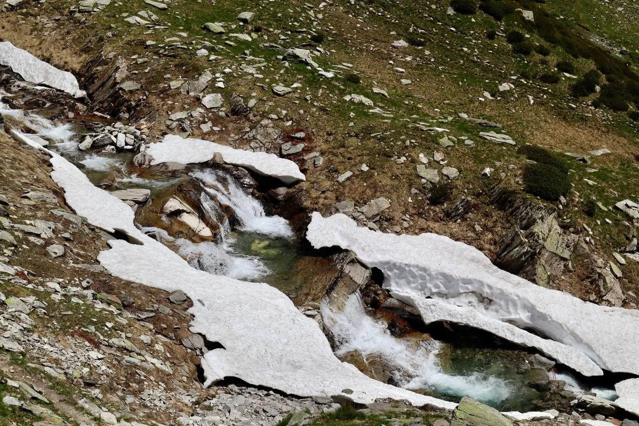 Mountain stream cascading under shrinking snow bridges in the Valle Canaria.