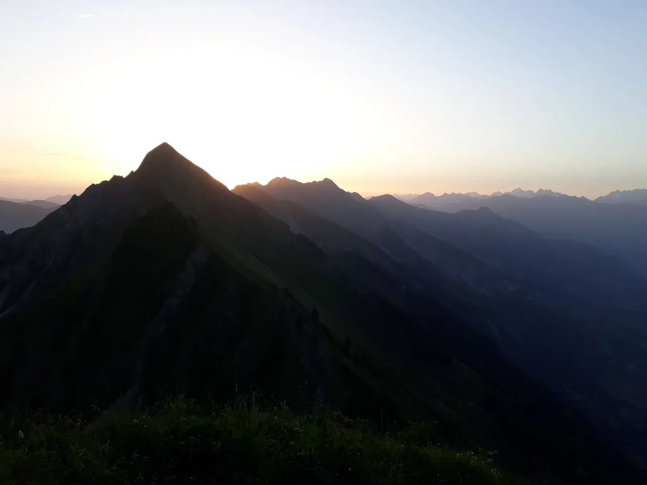 A sharp peak on the ridge silhouetted against the first light of dawn, ridge upon ridge fading into the haze.